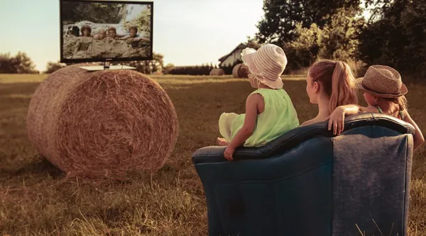 Familie sitzt im Freien vor einem Fernseher auf einem abgeernteten Feld