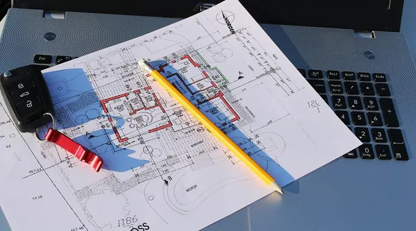 Bauplan mit Bleistift und Zirkel auf einem aufgeklappten Notebook