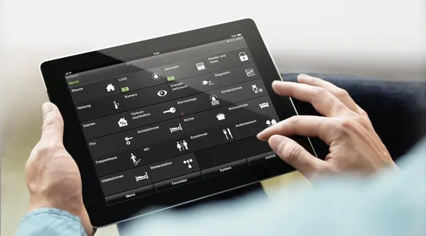 Hände bedienen ein Tablet mit der Raumübersicht einer Gebäudesteuerung