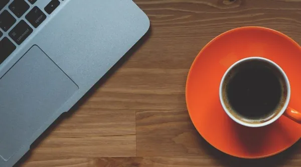 Aufgeklapptes Notebook und eine Tasse Kaffee auf einem Holztisch