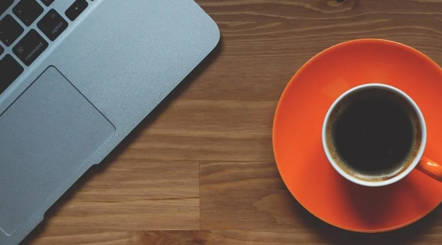 Aufgeklapptes Notebook und eine Tasse Kaffee auf einem Holztisch