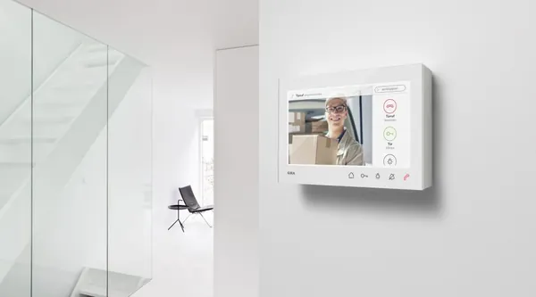 Videosprechanlage an einer Wand zeigt einen Besucher mit Paket an der Haustür
